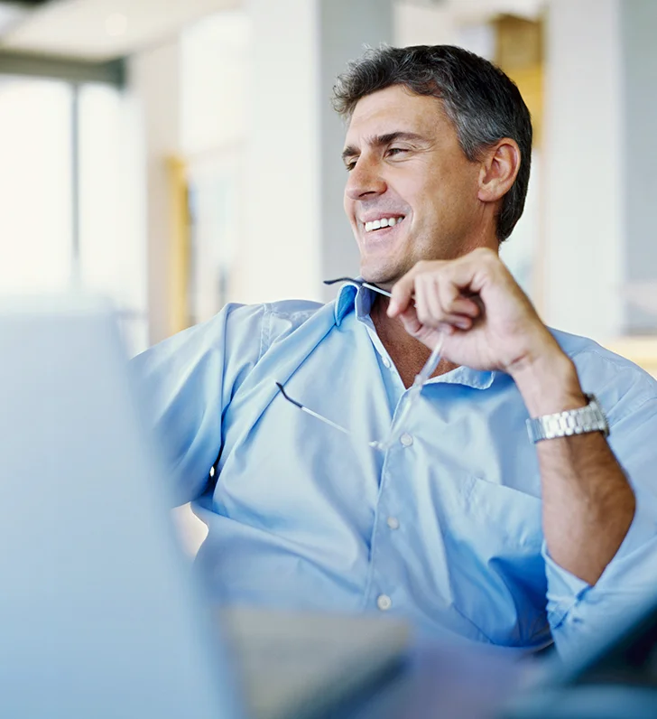 Man wearing blur shirt and smiling A man sitting in front of a laptop computer.
