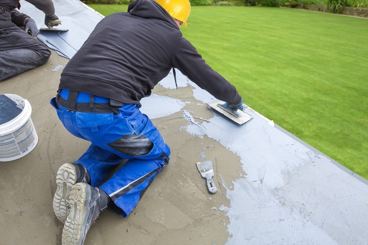 A man in blue pants and yellow hard hat working on the roof of a house.