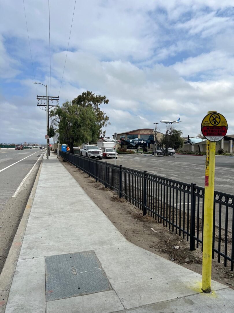 Sidewalk with black fence and warning sign.