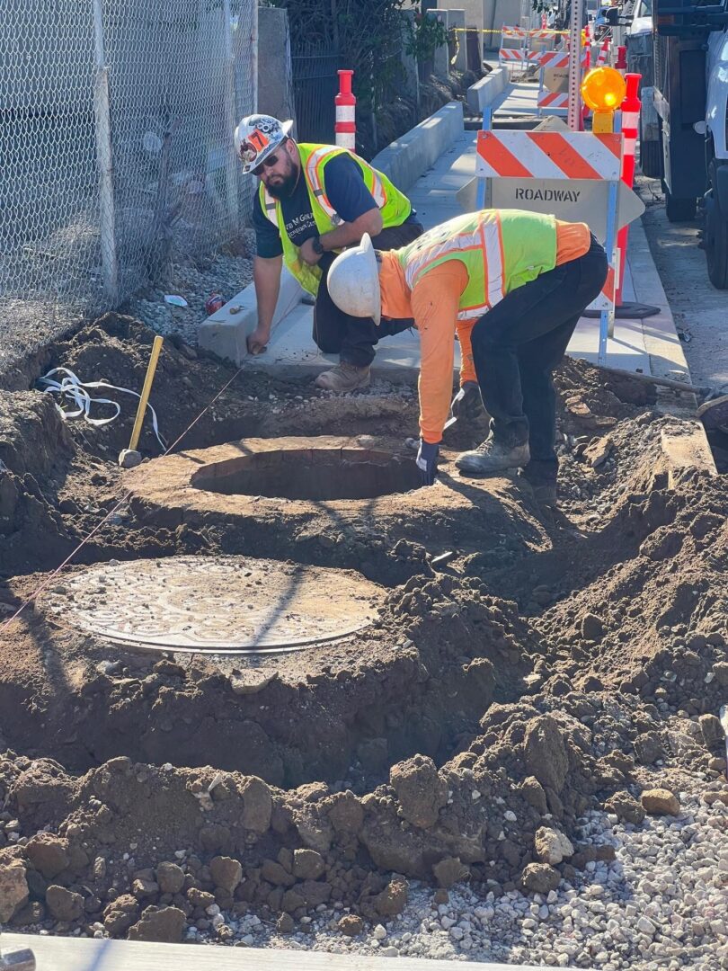 Two construction workers near an open manhole.