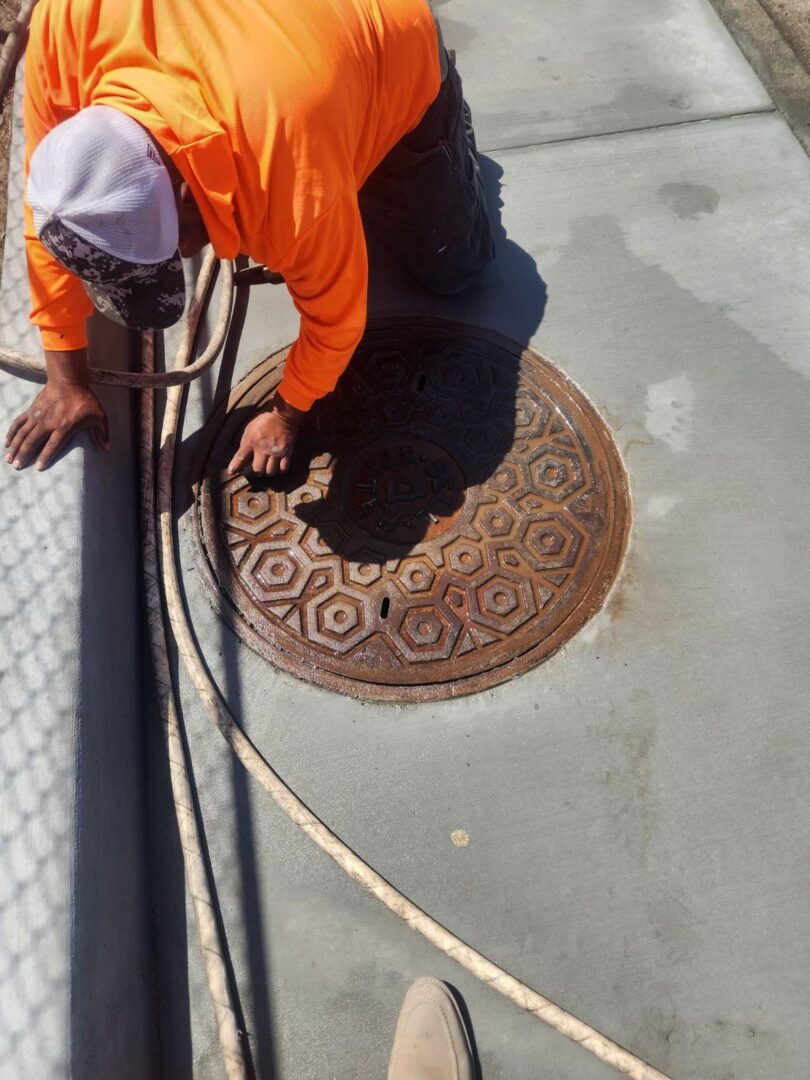 Person in orange inspecting manhole cover.