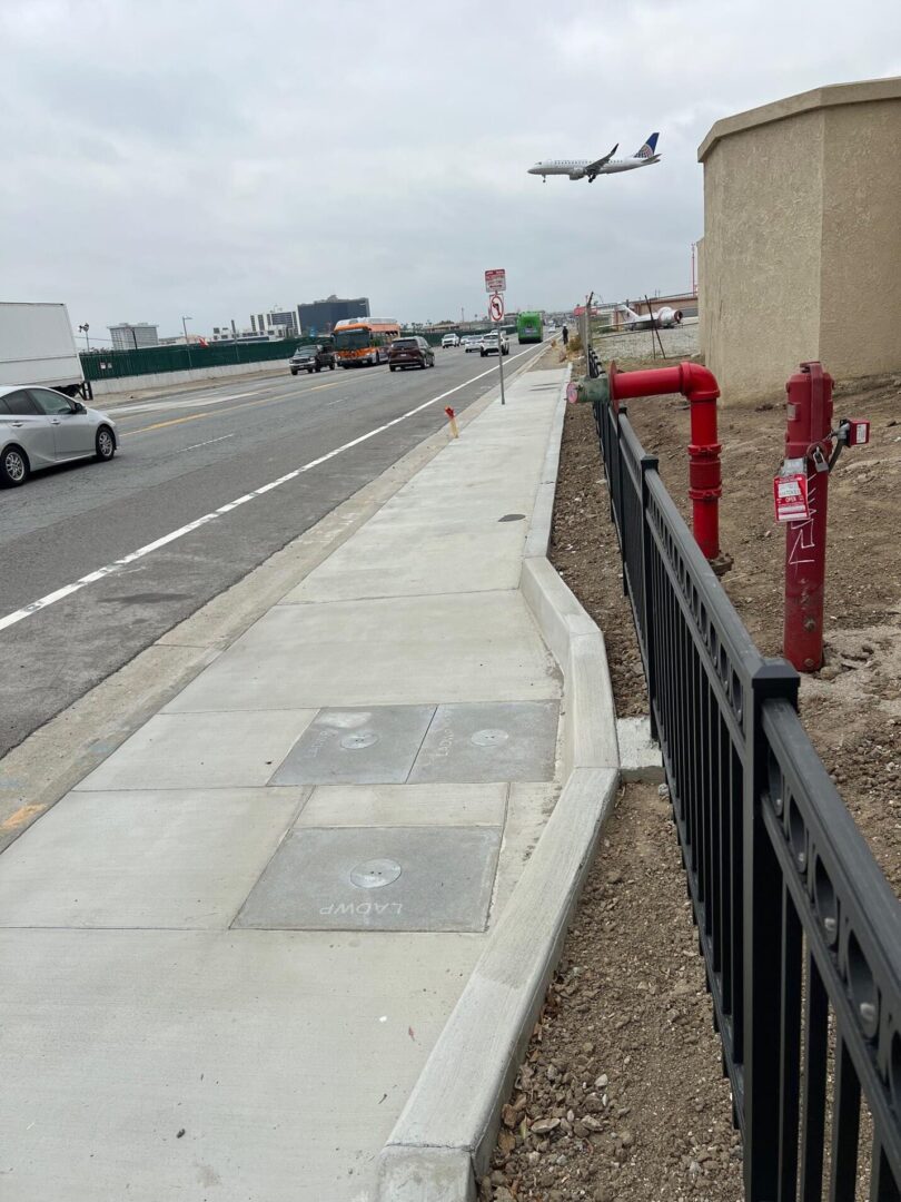 Sidewalk next to black fence with plane overhead.