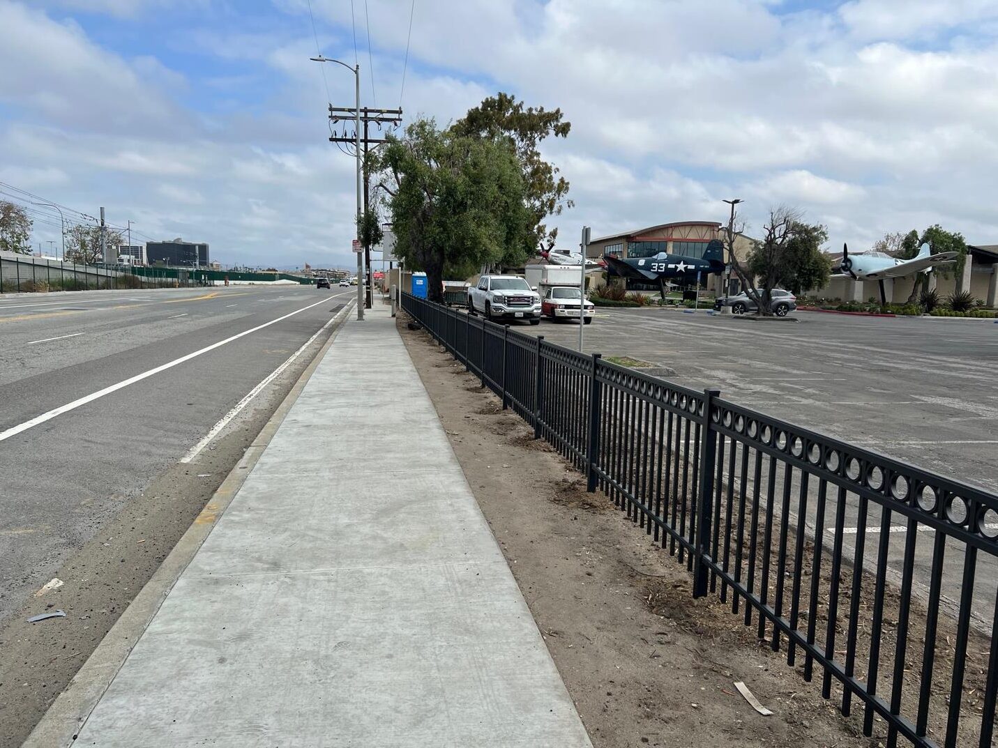 Sidewalk, fence, road, and airplane.