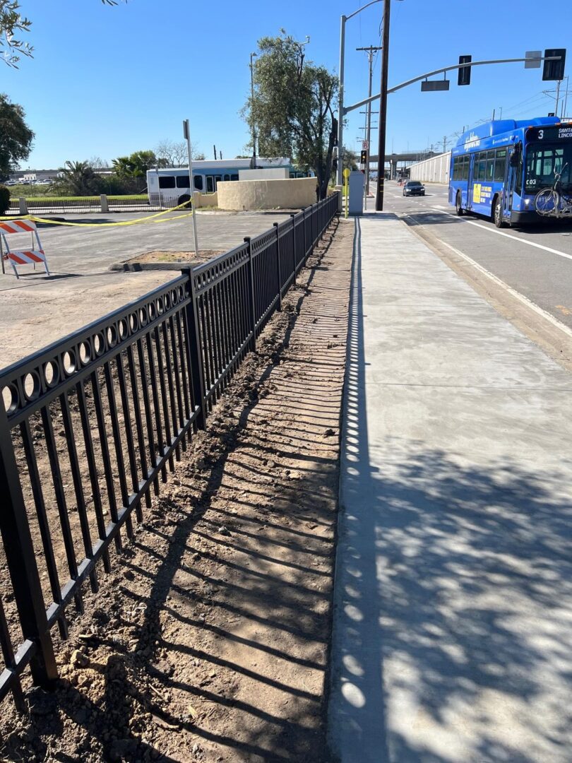 Black fence and sidewalk with shadows.