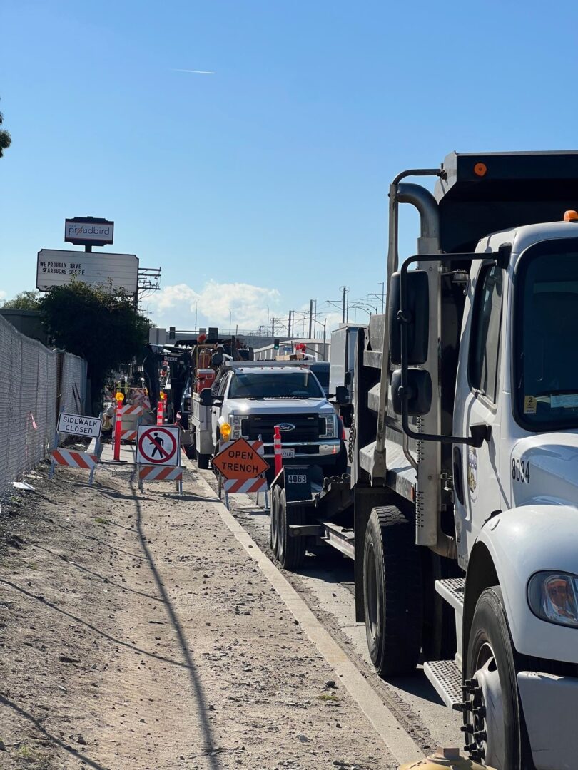 Construction trucks on road with open trench signs.